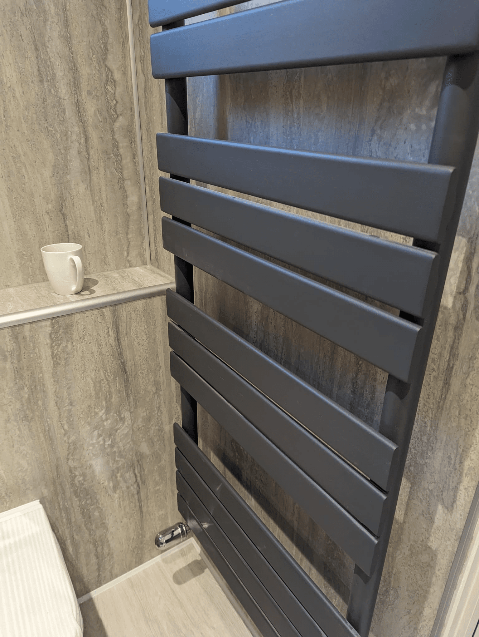 Anthracite flat-panel heated towel rail mounted on large-format grey stone-effect tiles