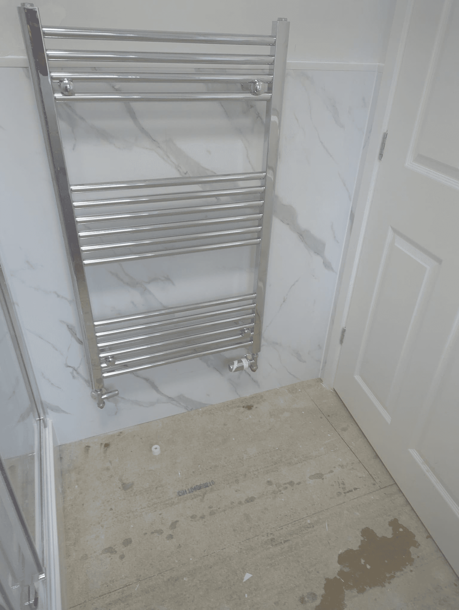 Chrome ladder heated towel rail fitted against white marble-effect wall panels