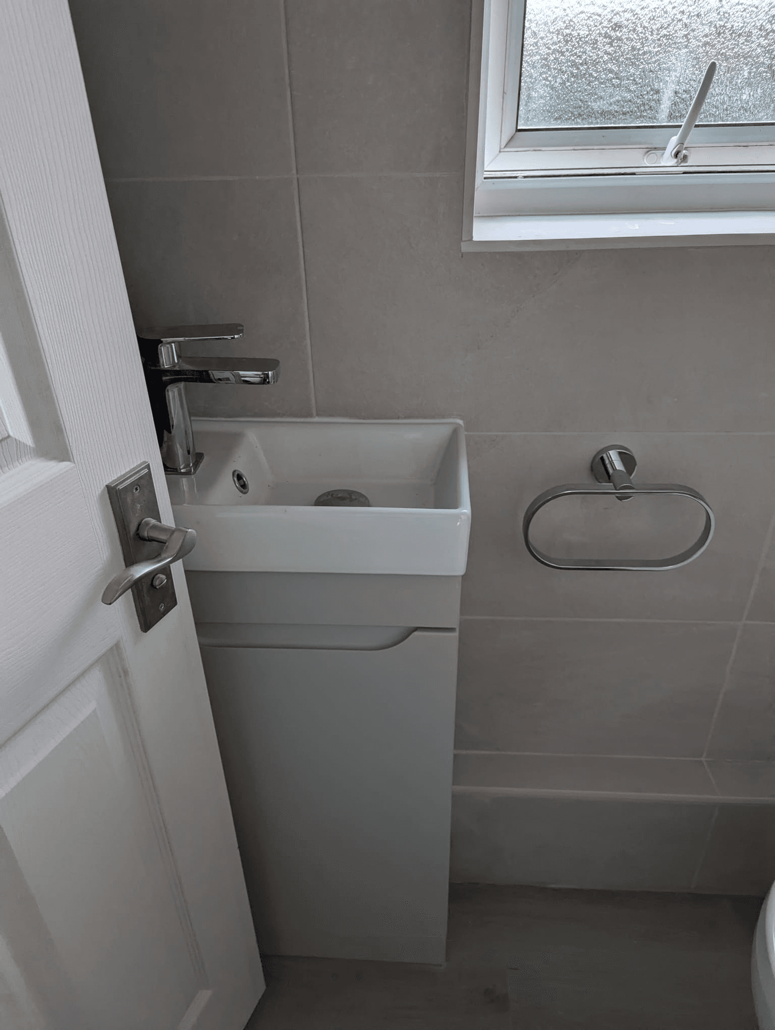 Compact cloakroom with wall-hung mini basin, tall chrome tap and chrome towel ring on grey tiles