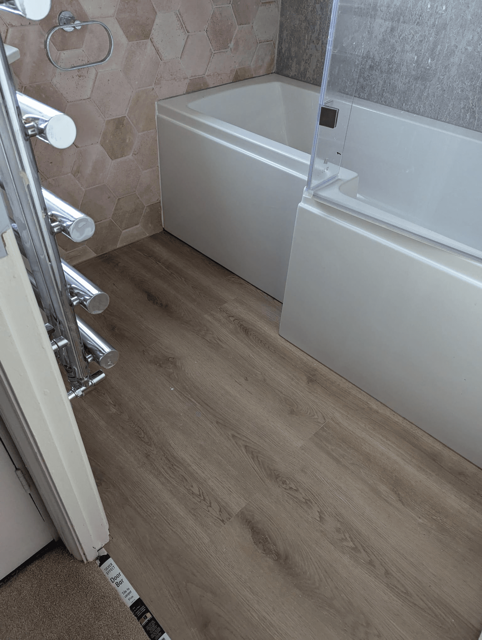 Bathroom showing blush pink hexagon tiles with wood-effect LVT floor and chrome heated towel rail