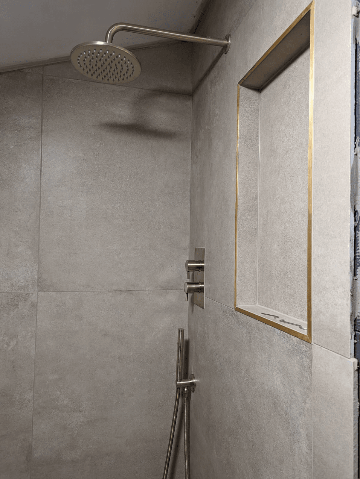 Ceiling rainfall shower head with gold-framed recessed niche shelf and concrete-look tiles