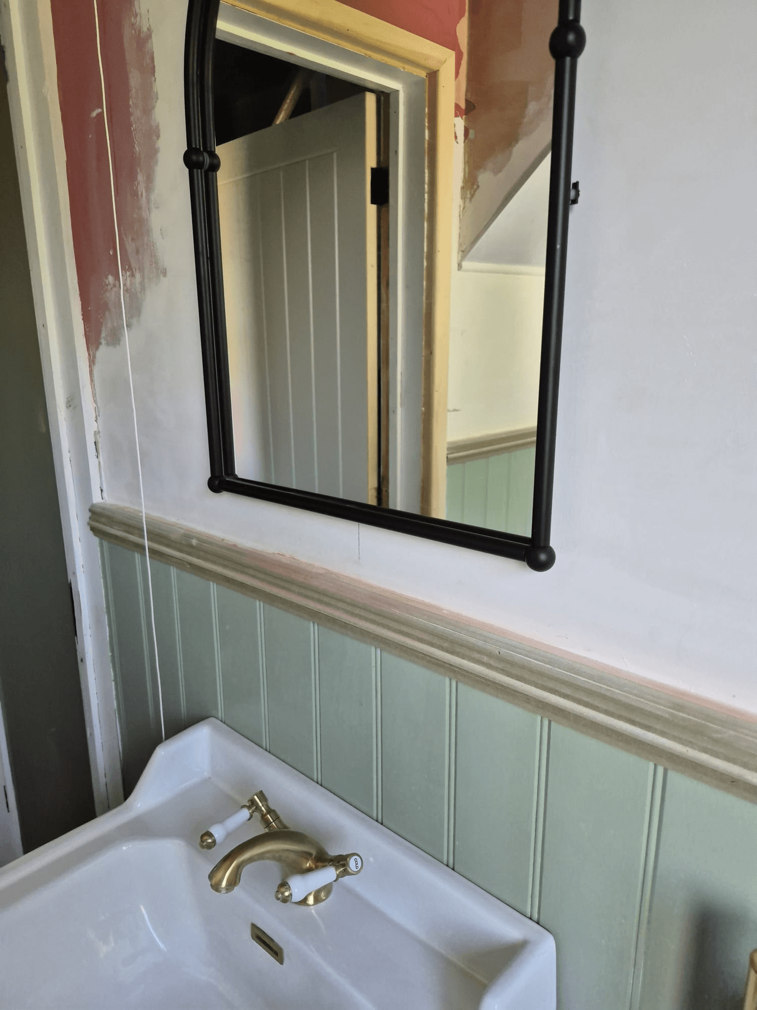 Sage green tongue-and-groove wall panelling with brass basin taps and black-framed mirror