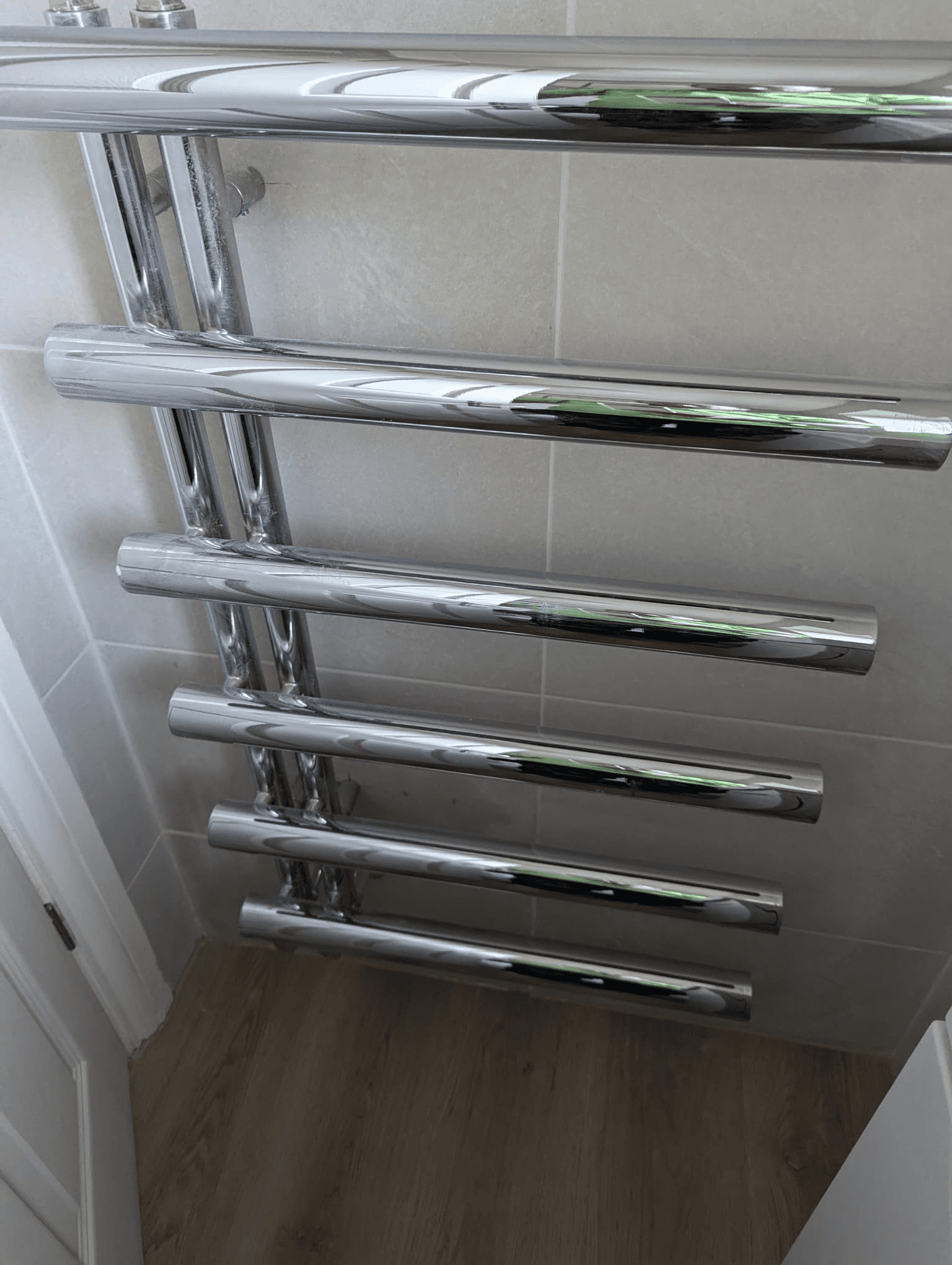 Large polished chrome square-bar heated towel rail in corner of tiled bathroom