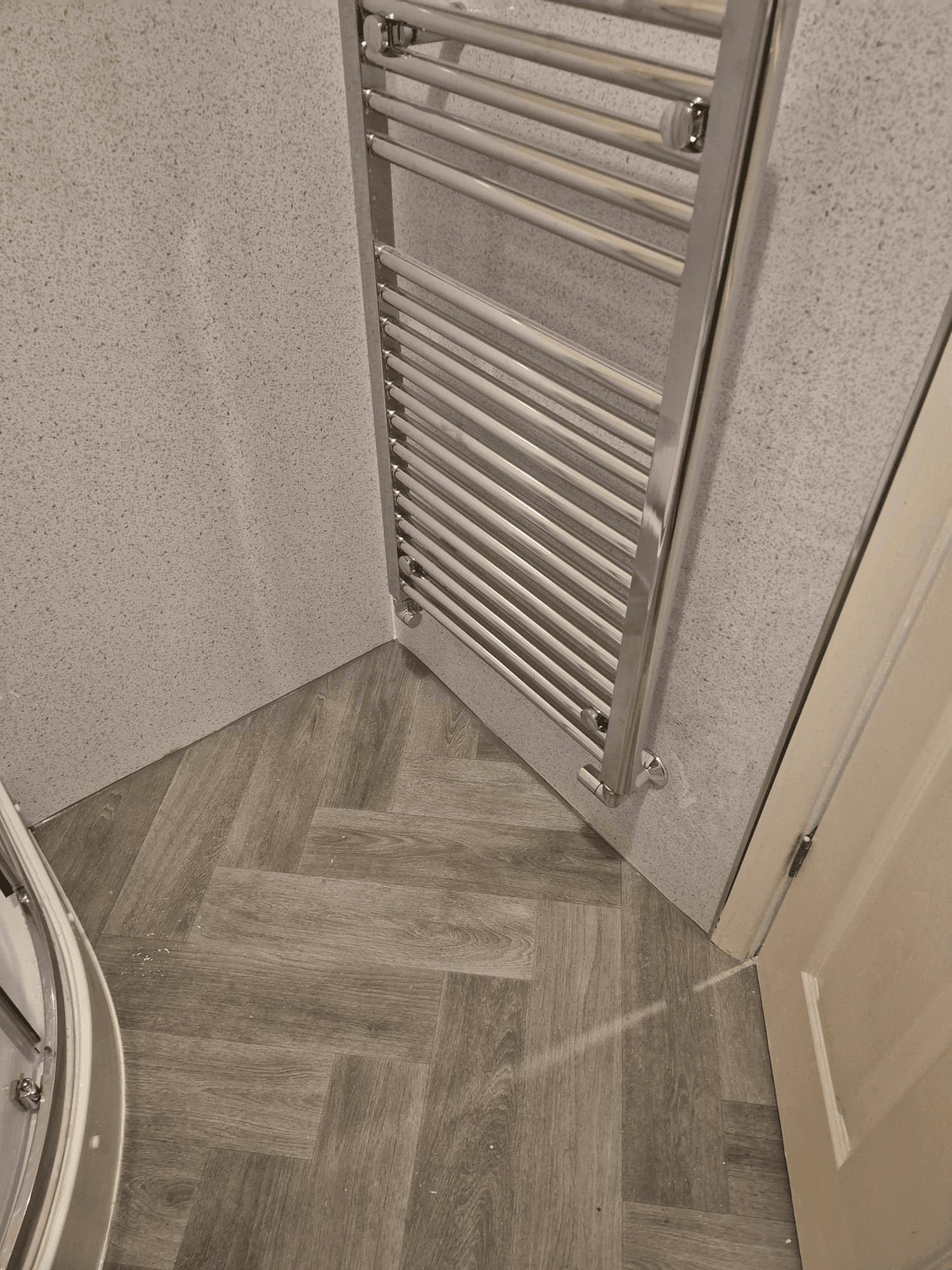 Chrome heated towel rail with herringbone vinyl floor tiles