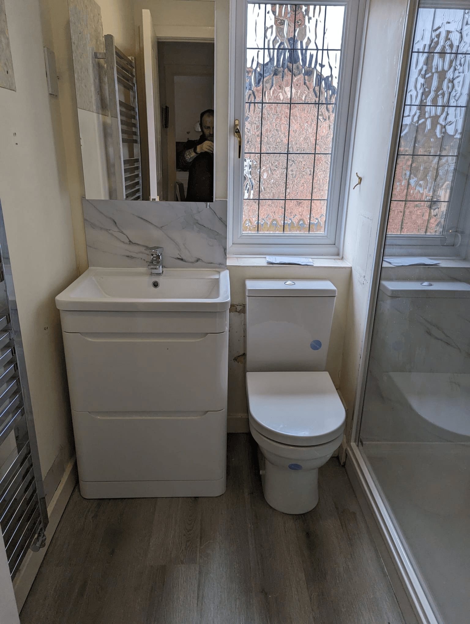 White vanity unit with marble-effect backsplash, close-coupled toilet and bath screen
