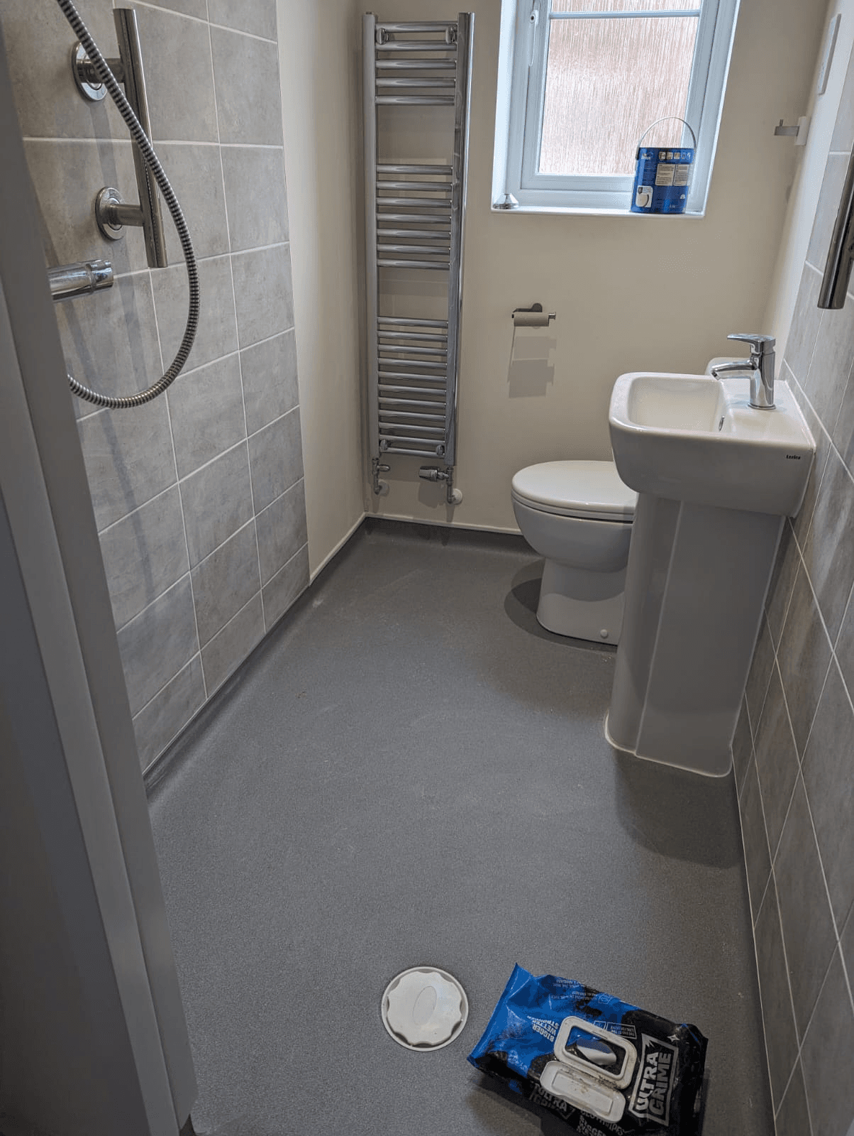 Wetroom with large grey floor-to-ceiling tiles, chrome heated towel rail, pedestal basin and toilet