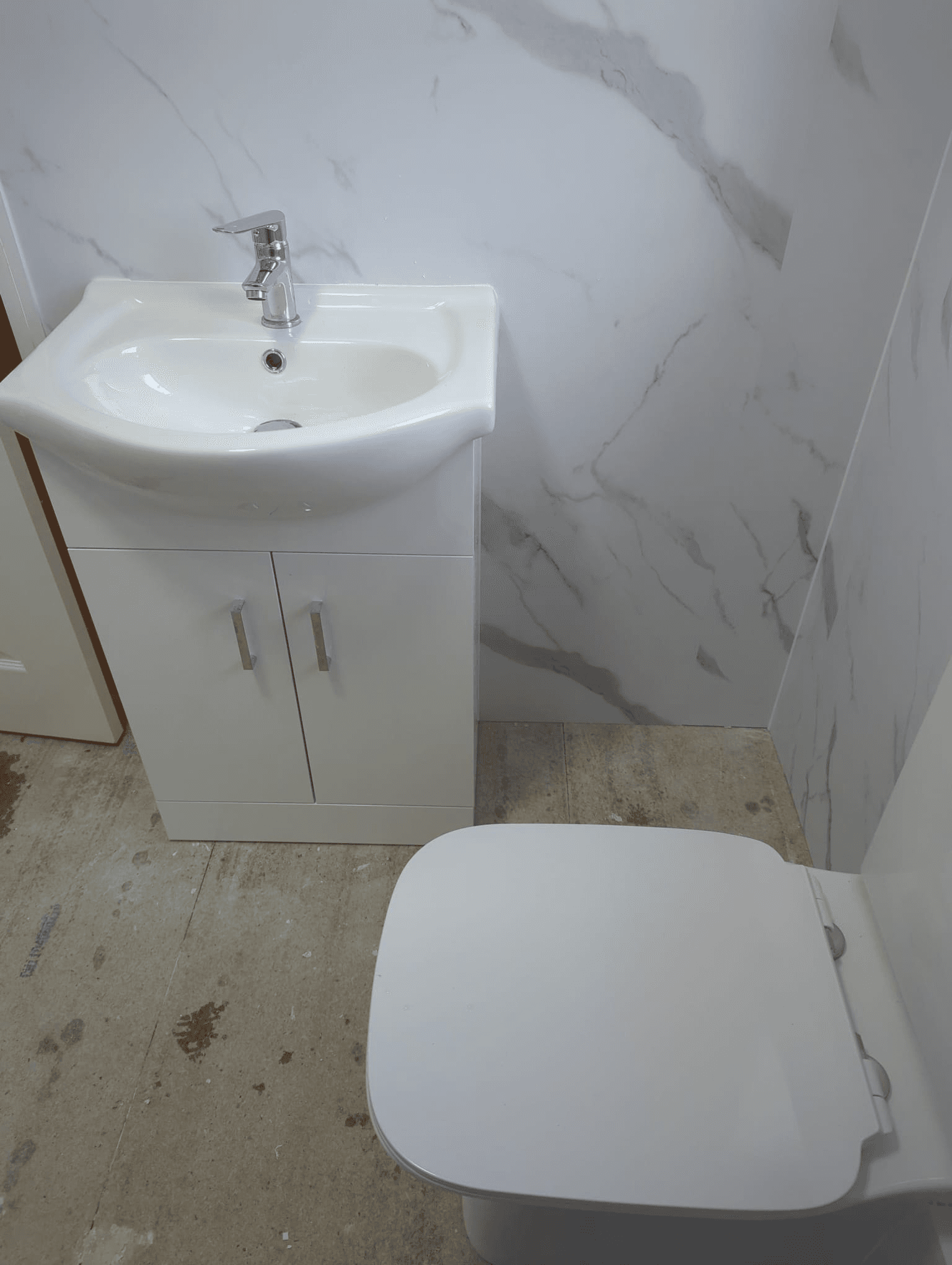 White floor-standing vanity unit with basin and close-coupled toilet against marble-effect panels